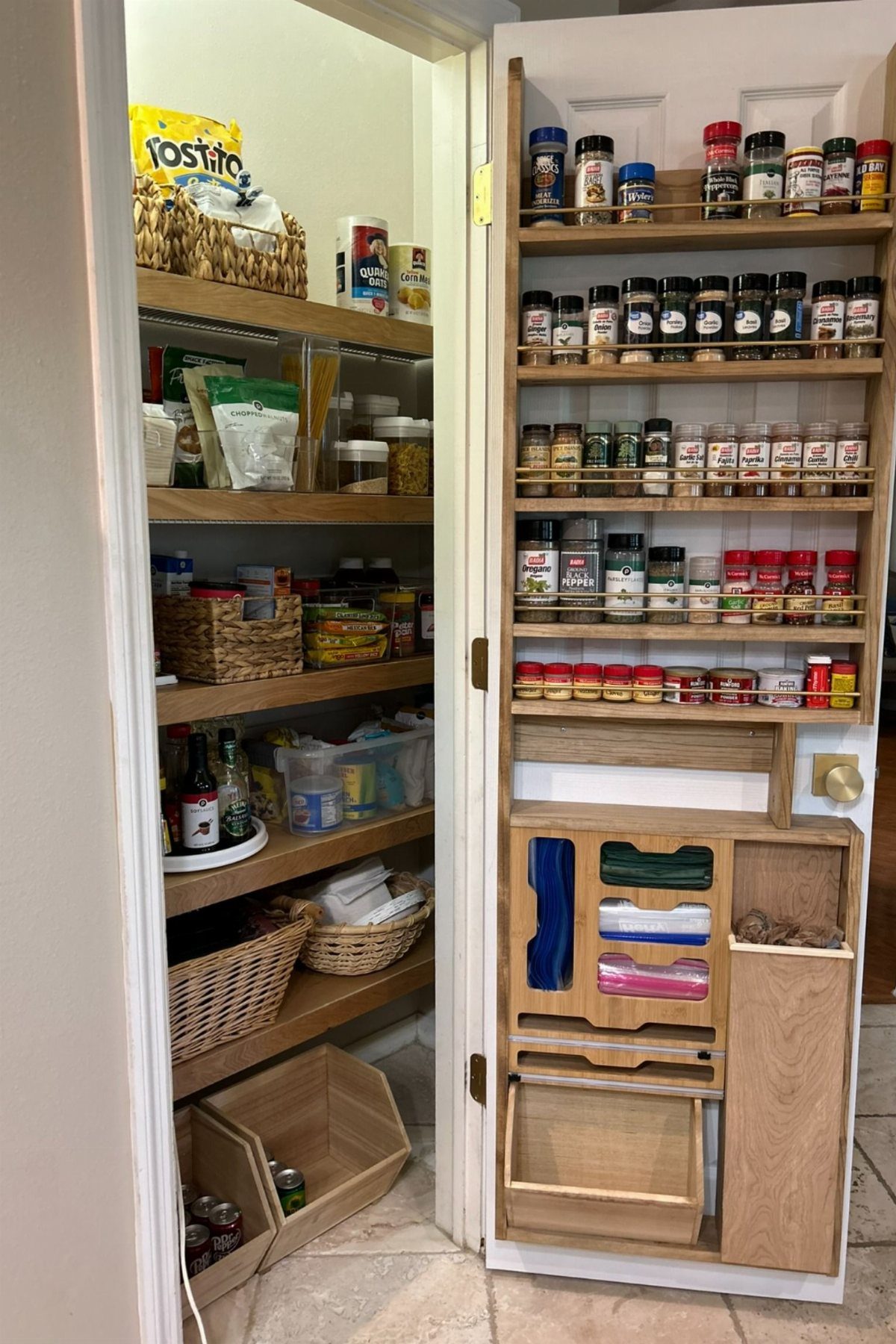 Light wood pull-out spice rack organizer attached to a white door in a pantry.