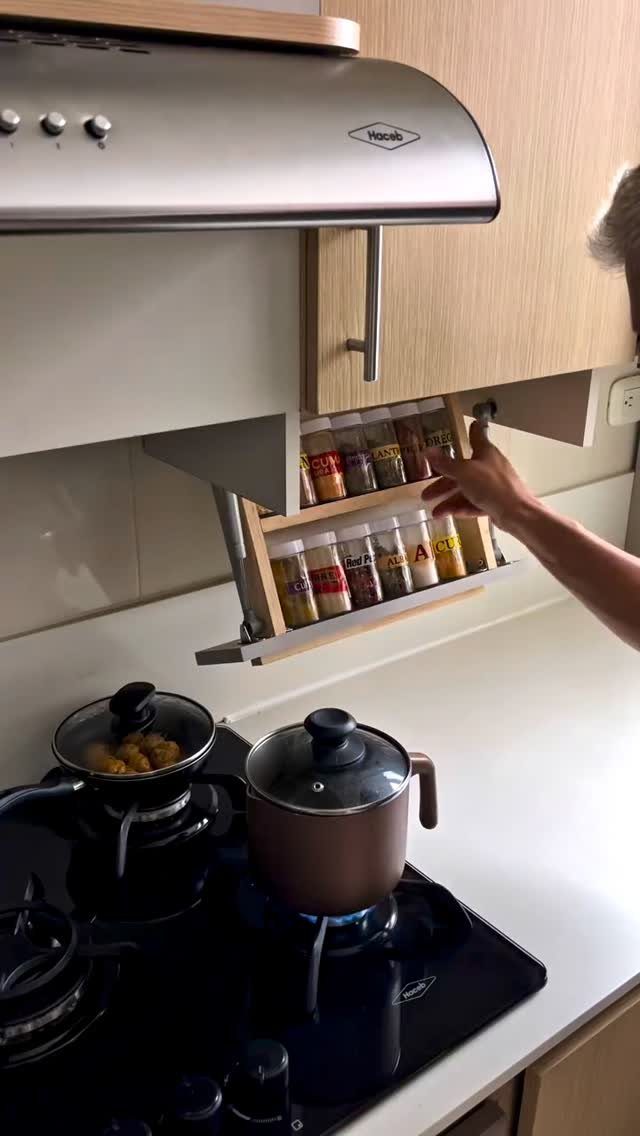 Wooden fold-down spice tray holding jars beneath a white kitchen cabinet near a stove.