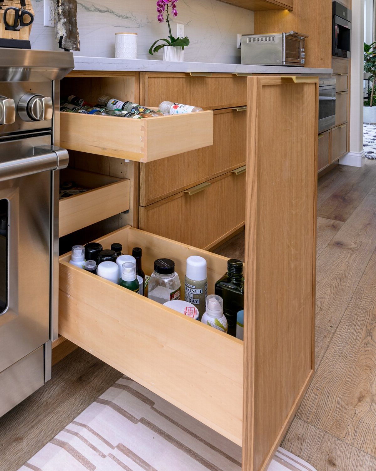 Light wood pull-out drawer organizer filled with spice jars in a kitchen cabinet.
