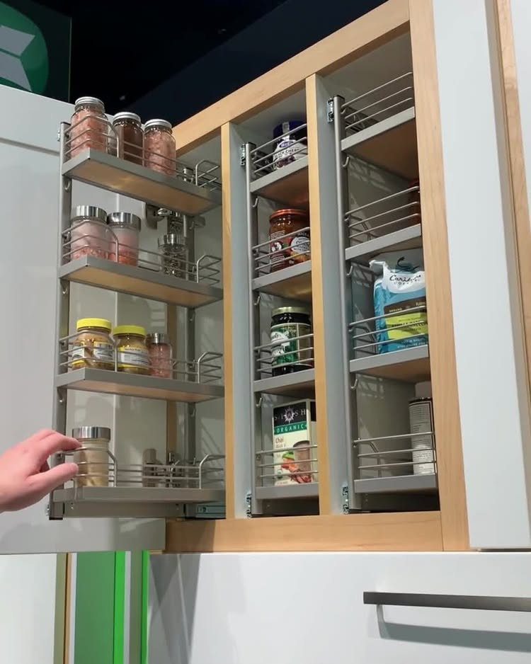 Pull-out maple cabinet spice rack with four tiers holding various glass jars.