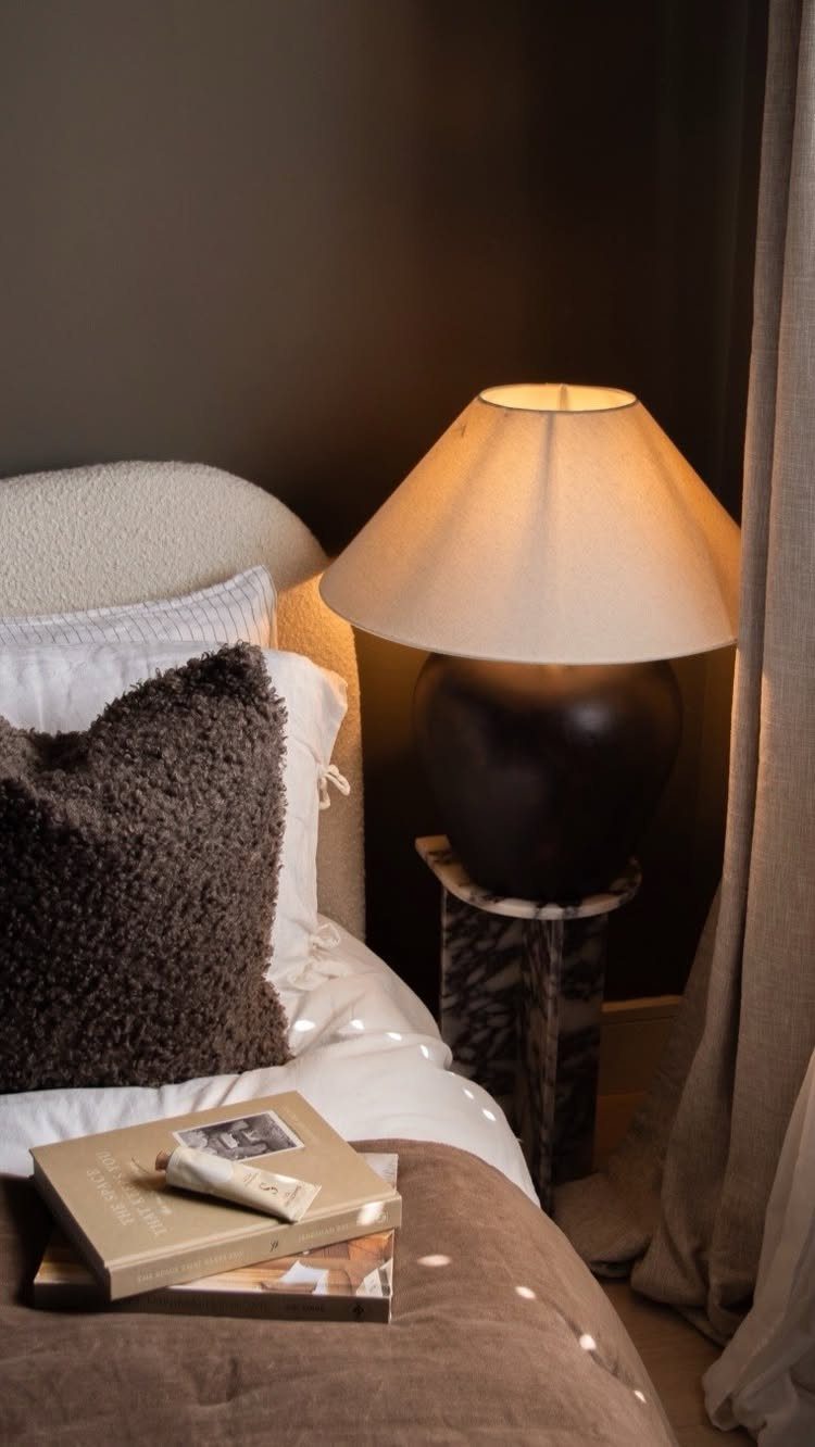 Bed with cream bedding and brown pillows against a dark chocolate brown wall.