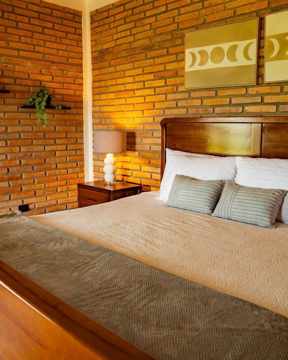Bedroom with red exposed brick walls, wooden bed frame, and neutral toned bedding.