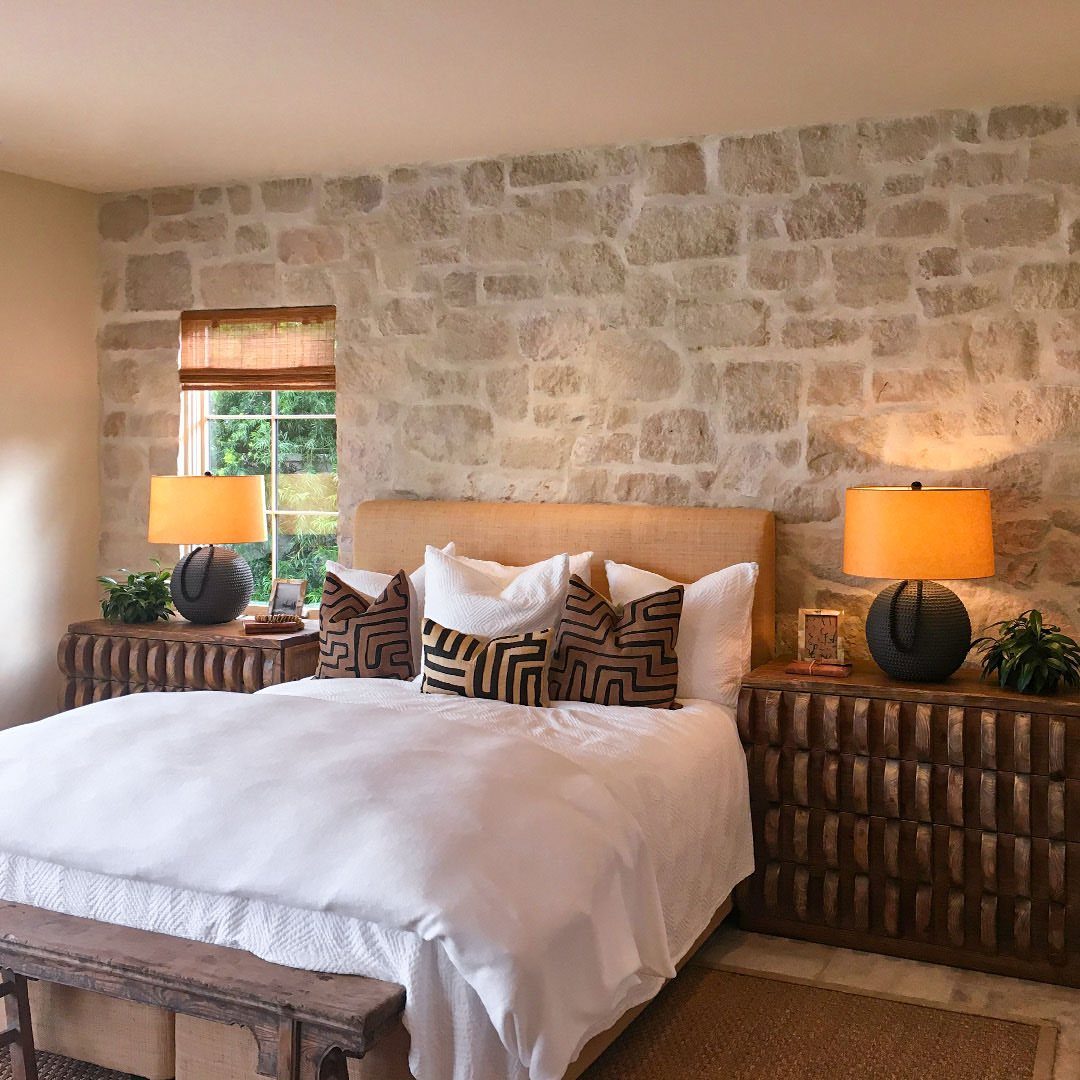 Stone accent wall in a rustic bedroom with white bedding and wooden furniture