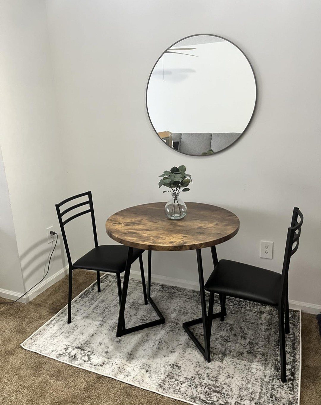 Small round rustic wood table with black metal legs and two black chairs.