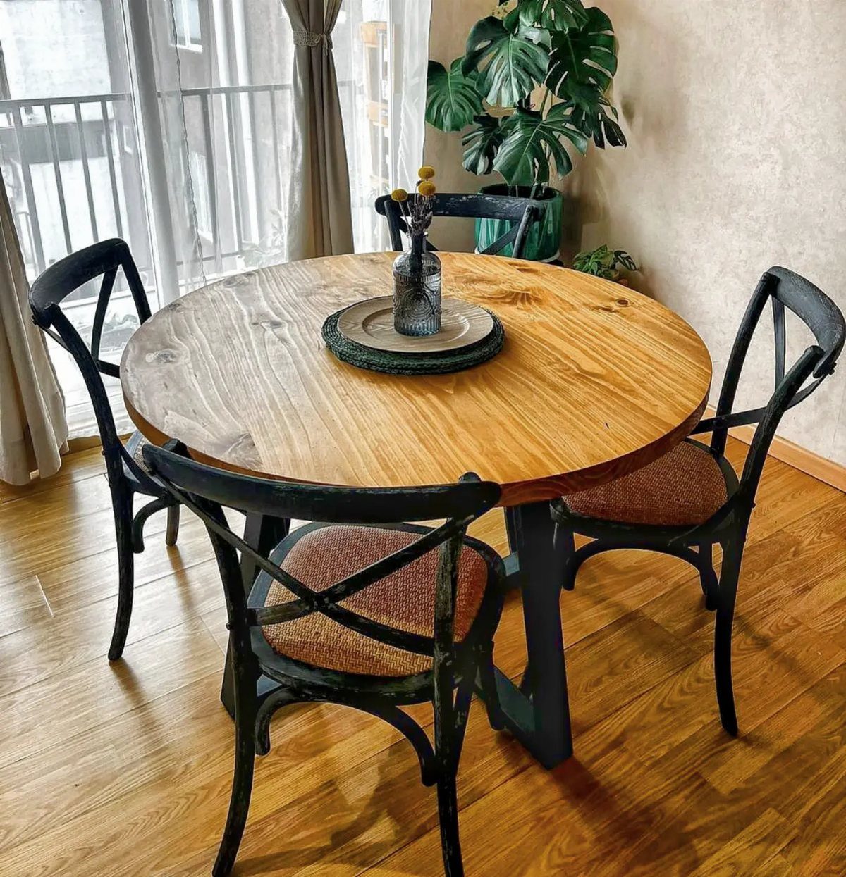 Round wooden dining table with black cross-back chairs on a hardwood floor.