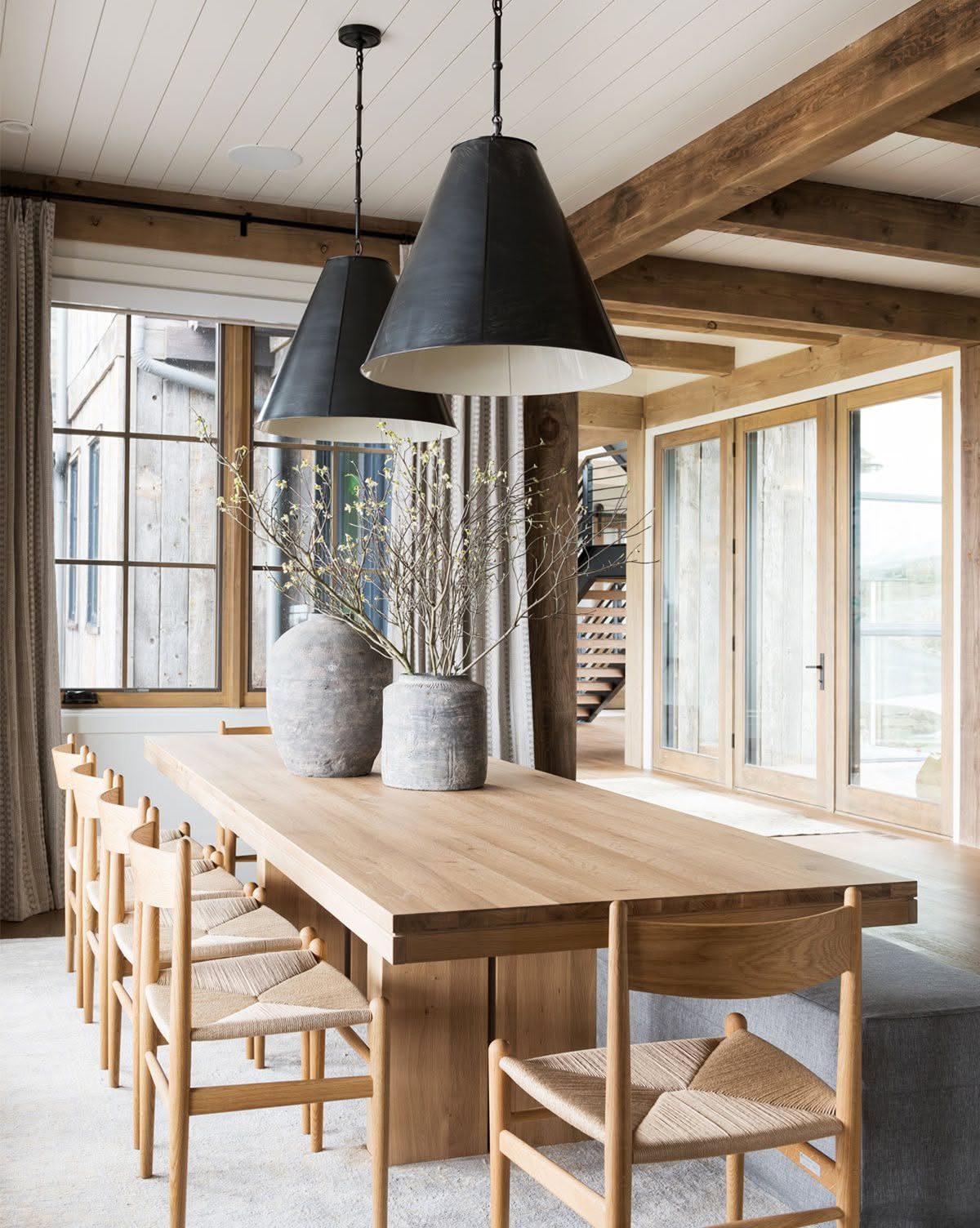 Long natural wood dining table with matching chairs under black conical pendant lights.