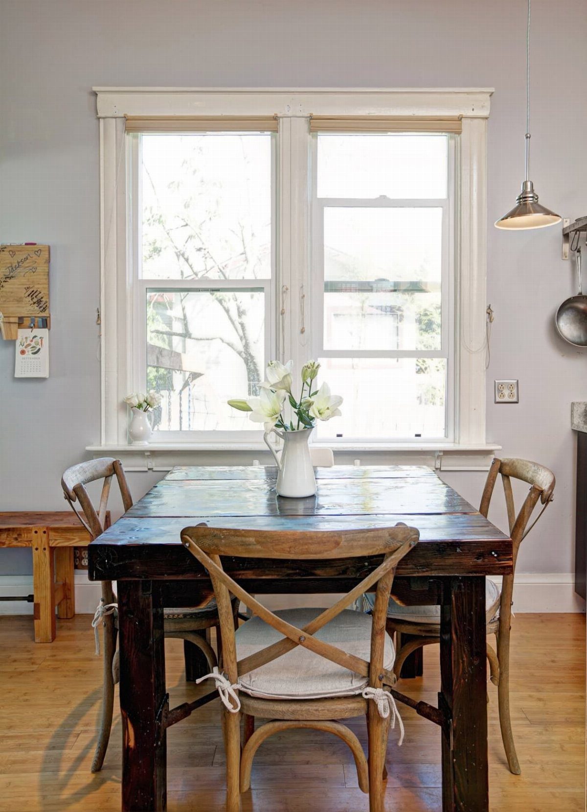 Dark wood dining table with light wood cross-back chairs and white cushions.