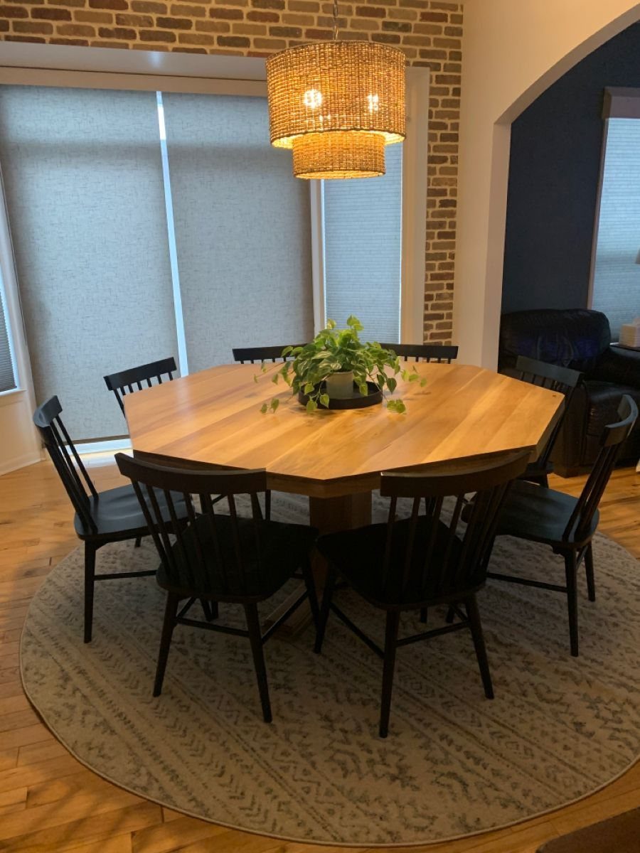 Octagonal wood dining table with black chairs and a woven pendant light above.