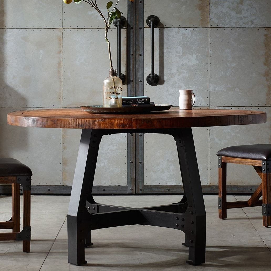 Round wooden dining table with a black industrial metal base and leather chairs.