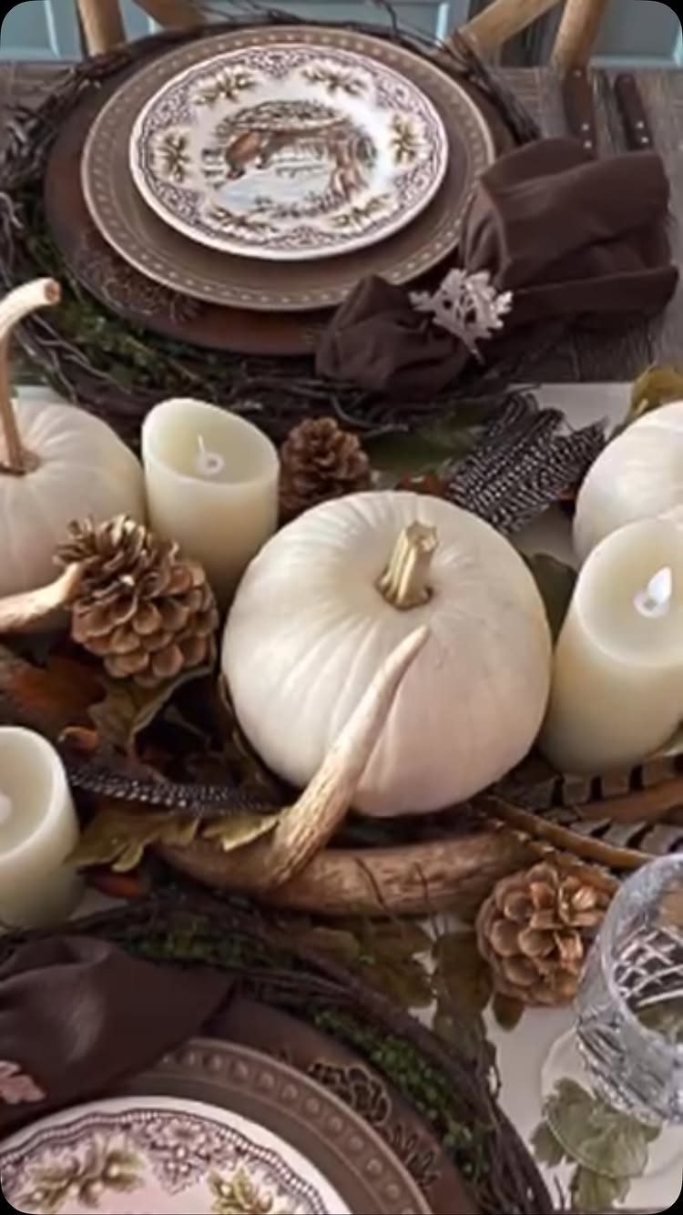 White pumpkins, pinecones, and candles arranged as a rustic fall centerpiece on a table.