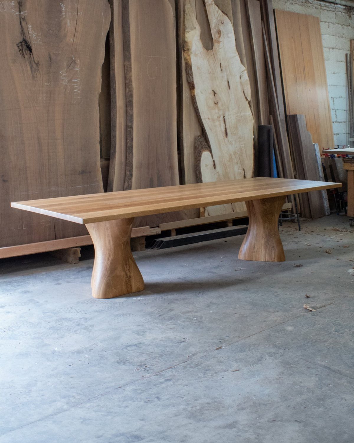 Natural wood dining table with thick curved sculptural bases in a woodworking shop