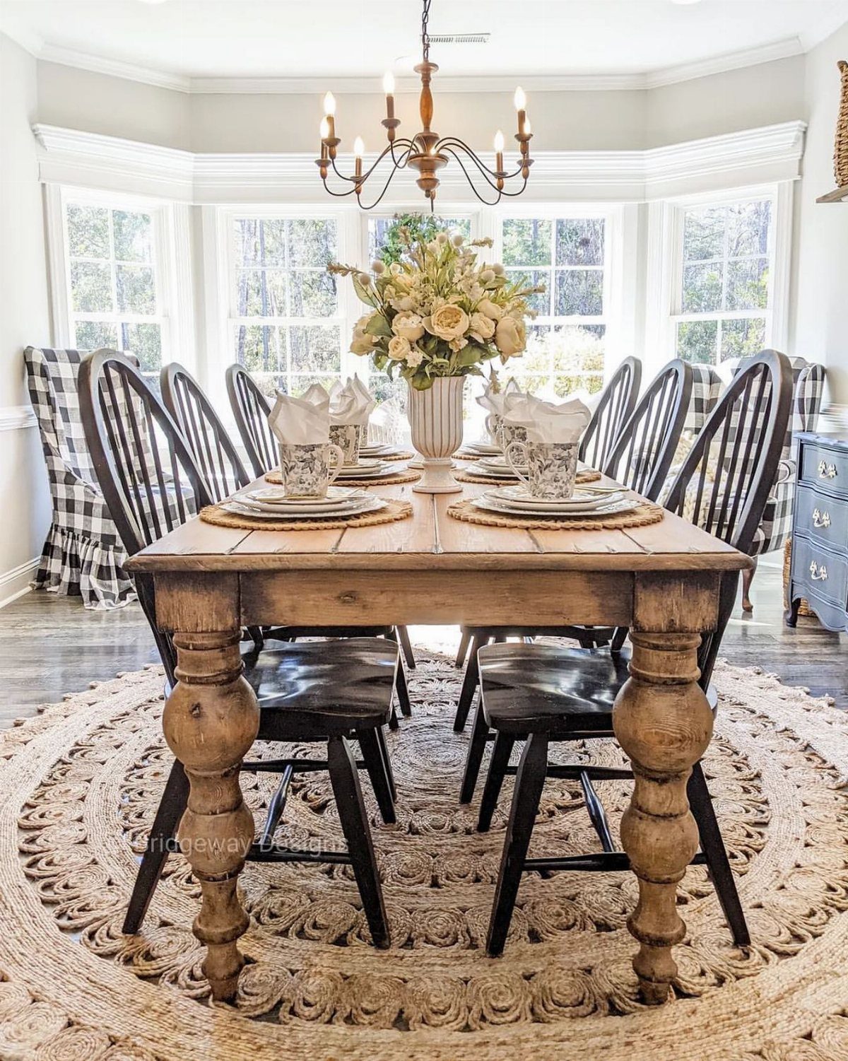Black spindle-back chairs around a rustic wooden dining table with a floral centerpiece.