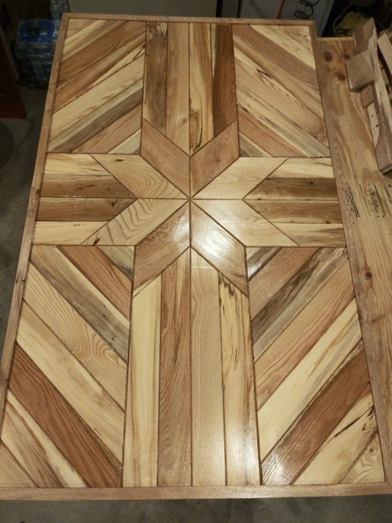 Wooden dining table top with a geometric star pattern made of inlaid planks.
