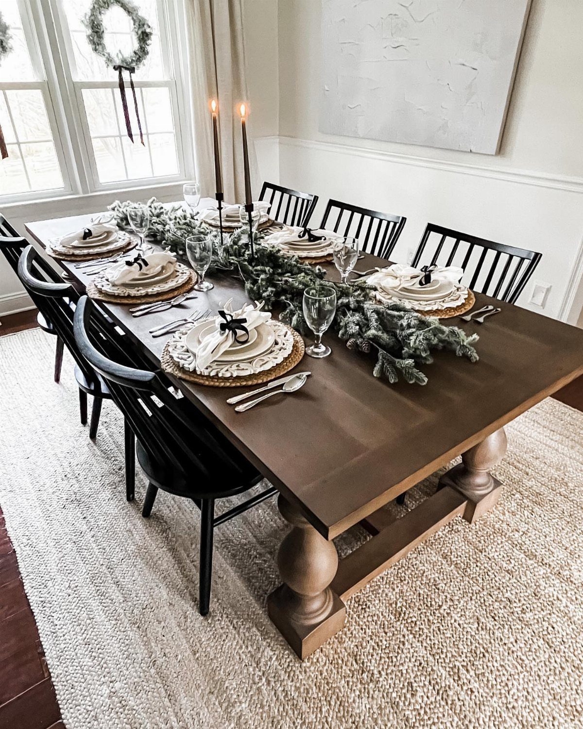 Wooden dining table with black chairs resting on a light-colored jute area rug.
