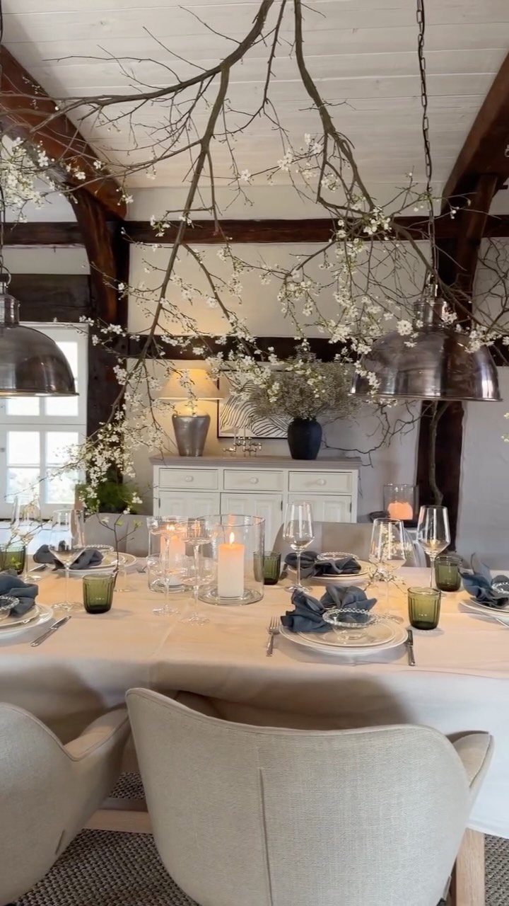 Dining table with white cloth and tall flowering seasonal branches reaching toward the ceiling.