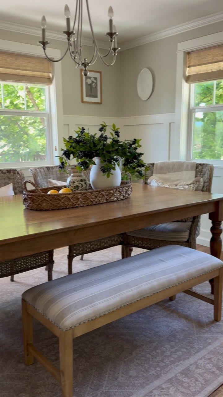 Rectangular wood dining table with a striped bench and wicker chairs in a bright room