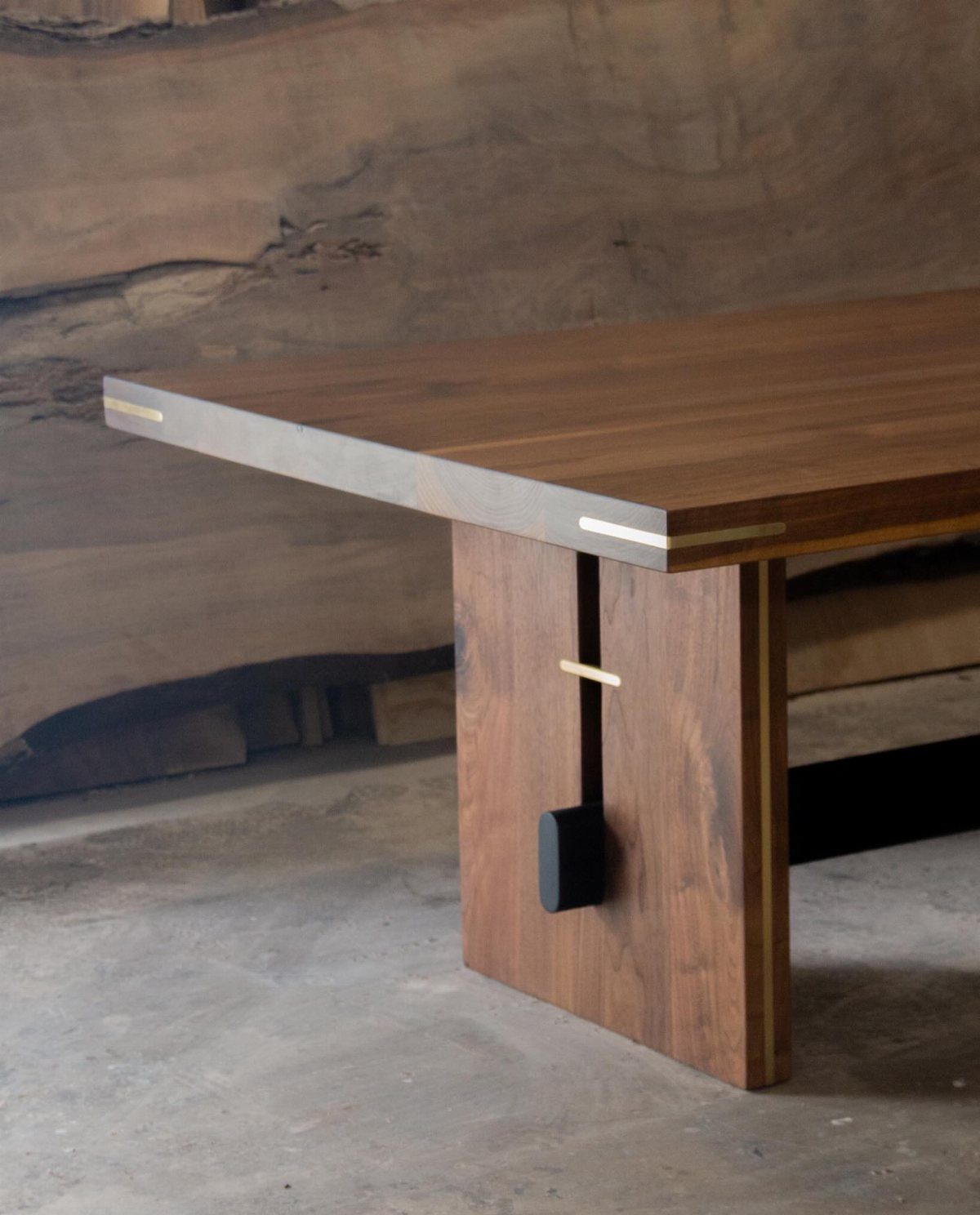 Walnut wood dining table with a thick slab leg and gold metal accents.