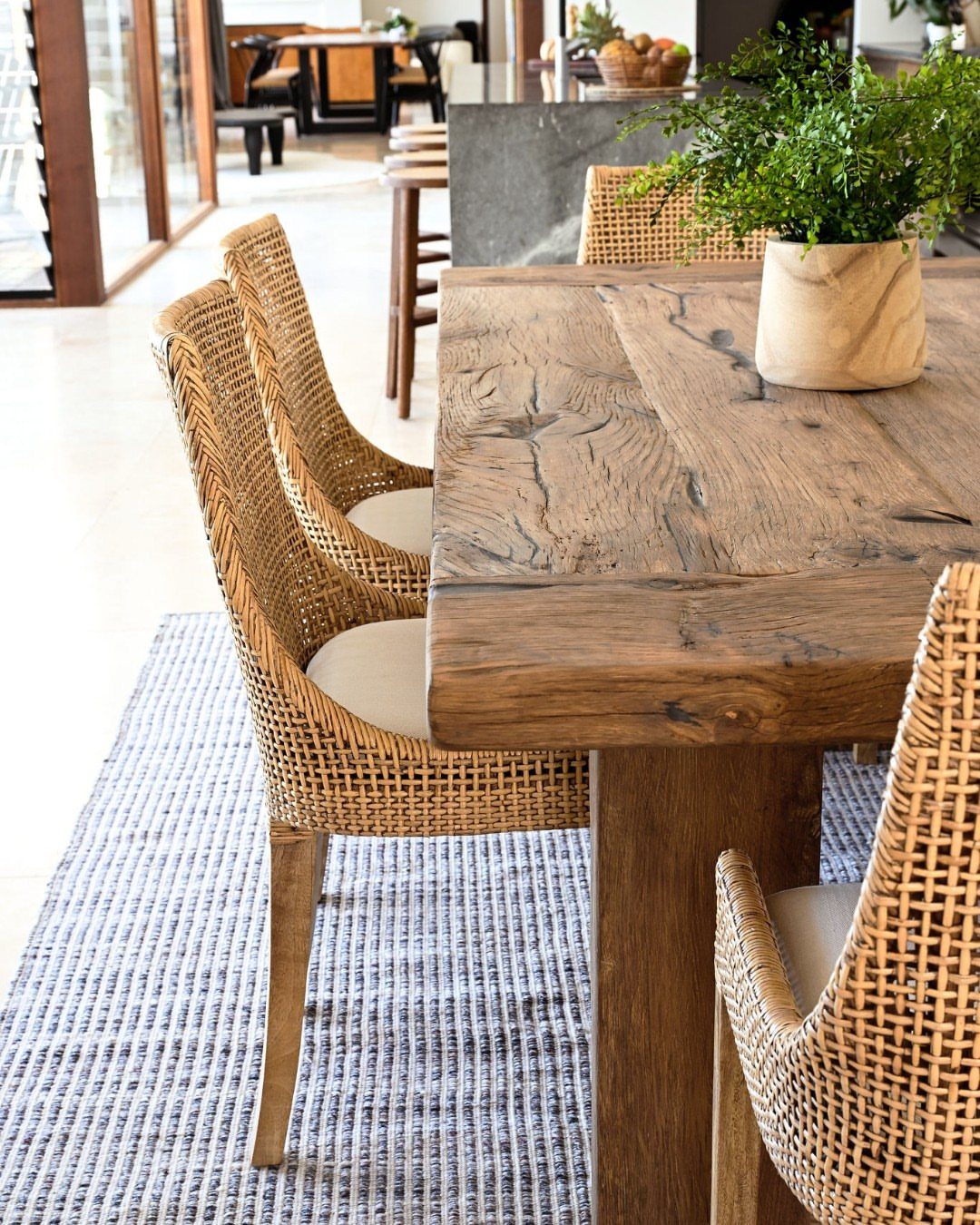 Rustic wooden dining table with woven wicker chairs and a potted plant on top.