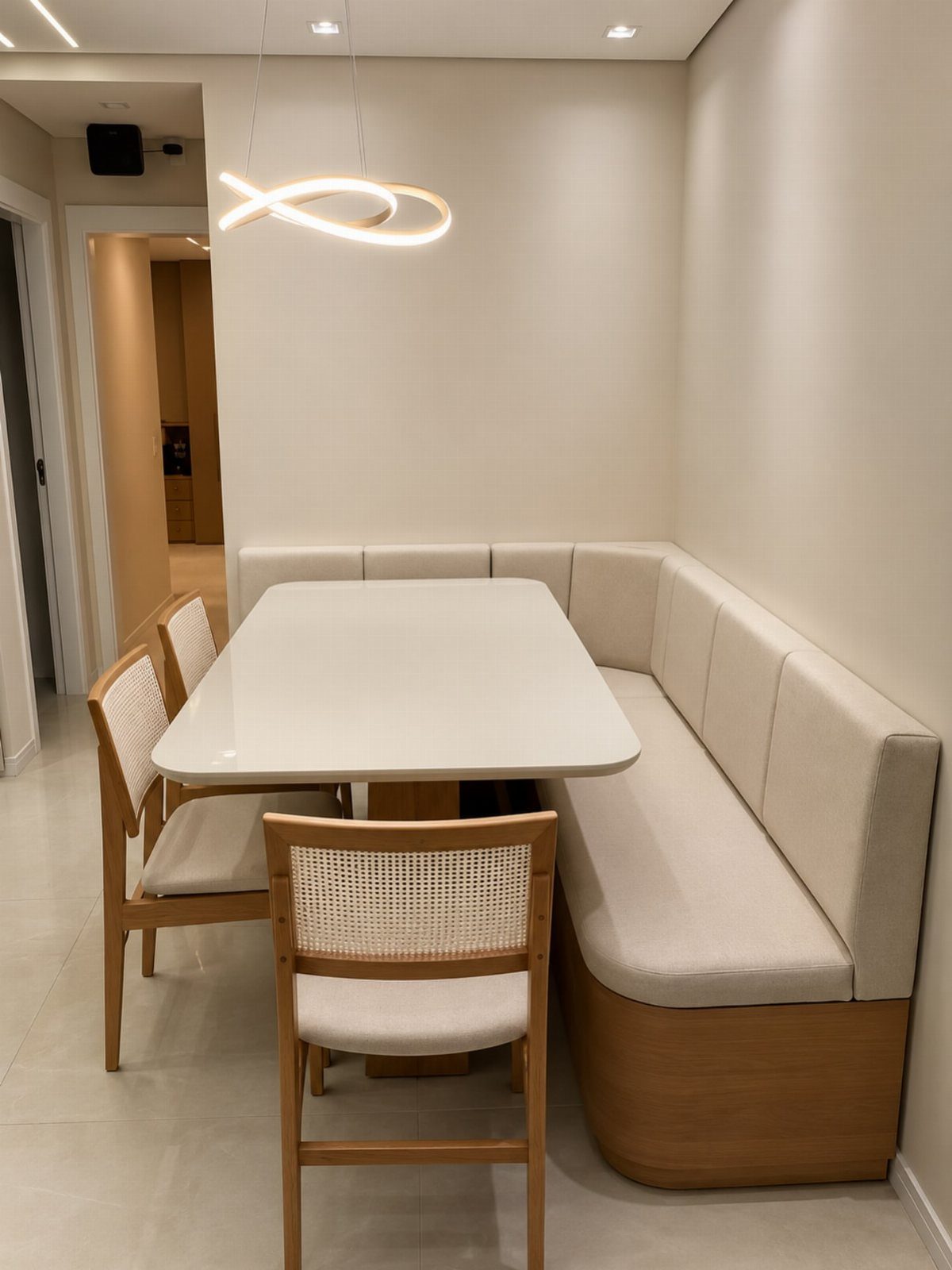 L-shaped built-in cream upholstered bench and white table in a minimalist dining area.