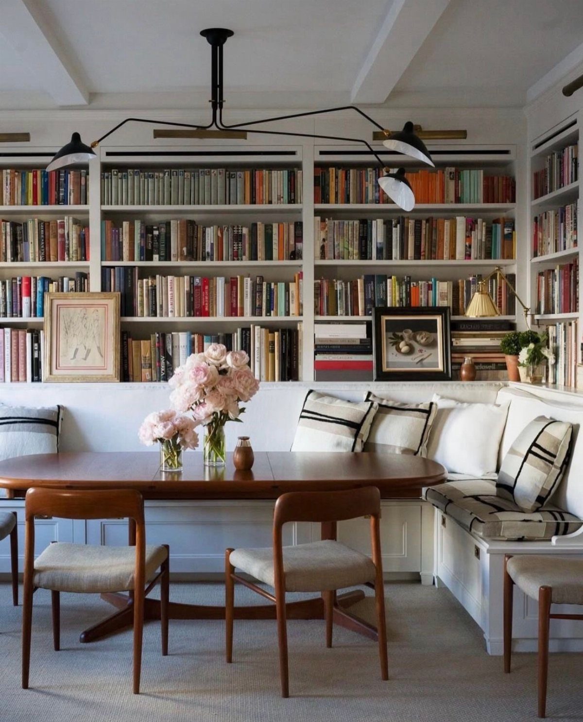 Oval wooden dining table and banquette seating positioned in front of white bookshelves.