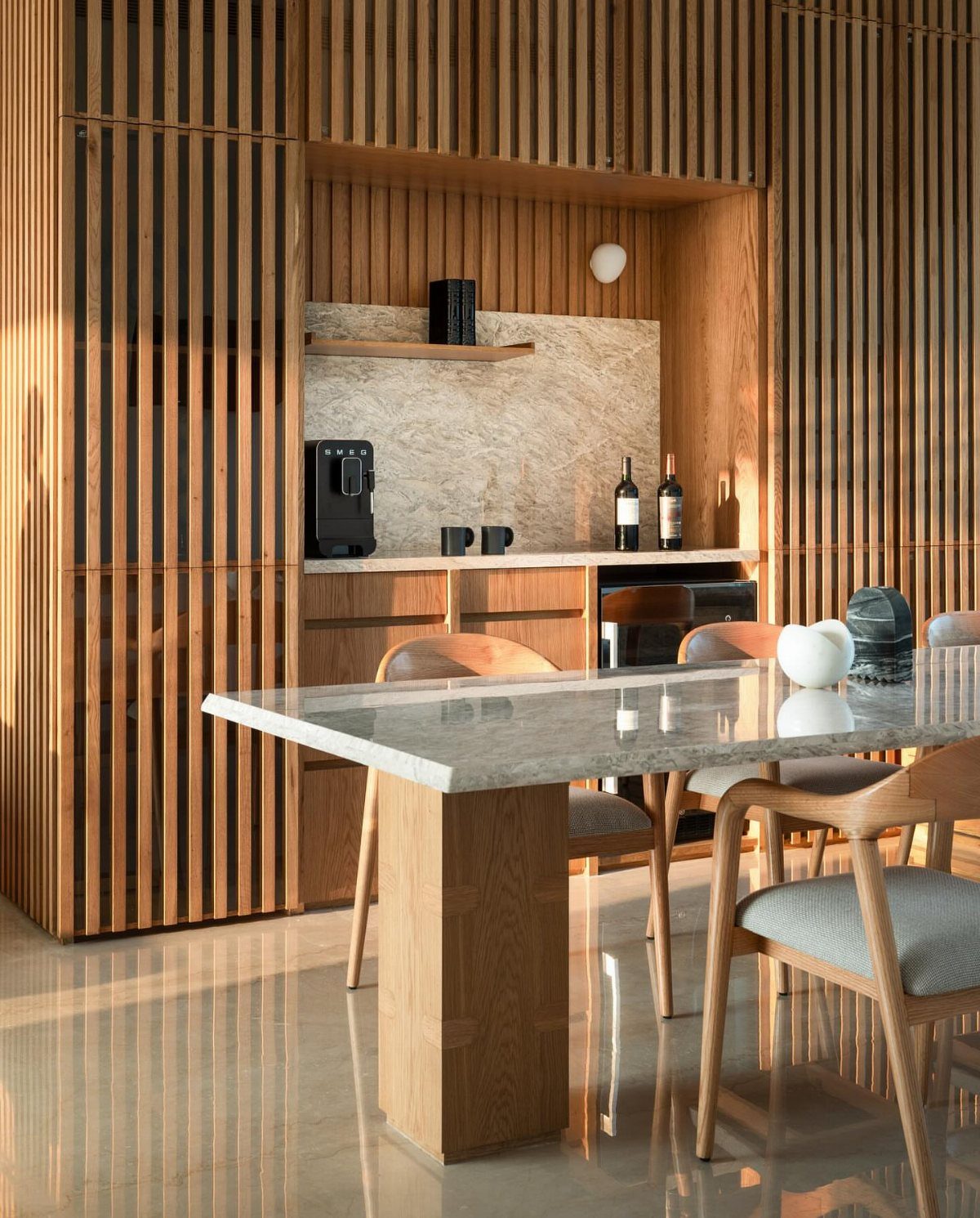 Marble-top dining table with wooden chairs in a room with vertical wood slats.
