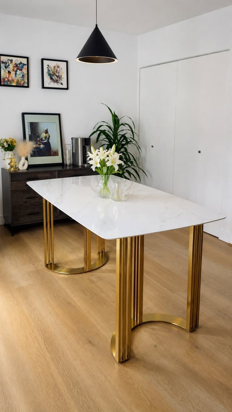 White rectangular dining table with gold legs in a bright, modern dining area.