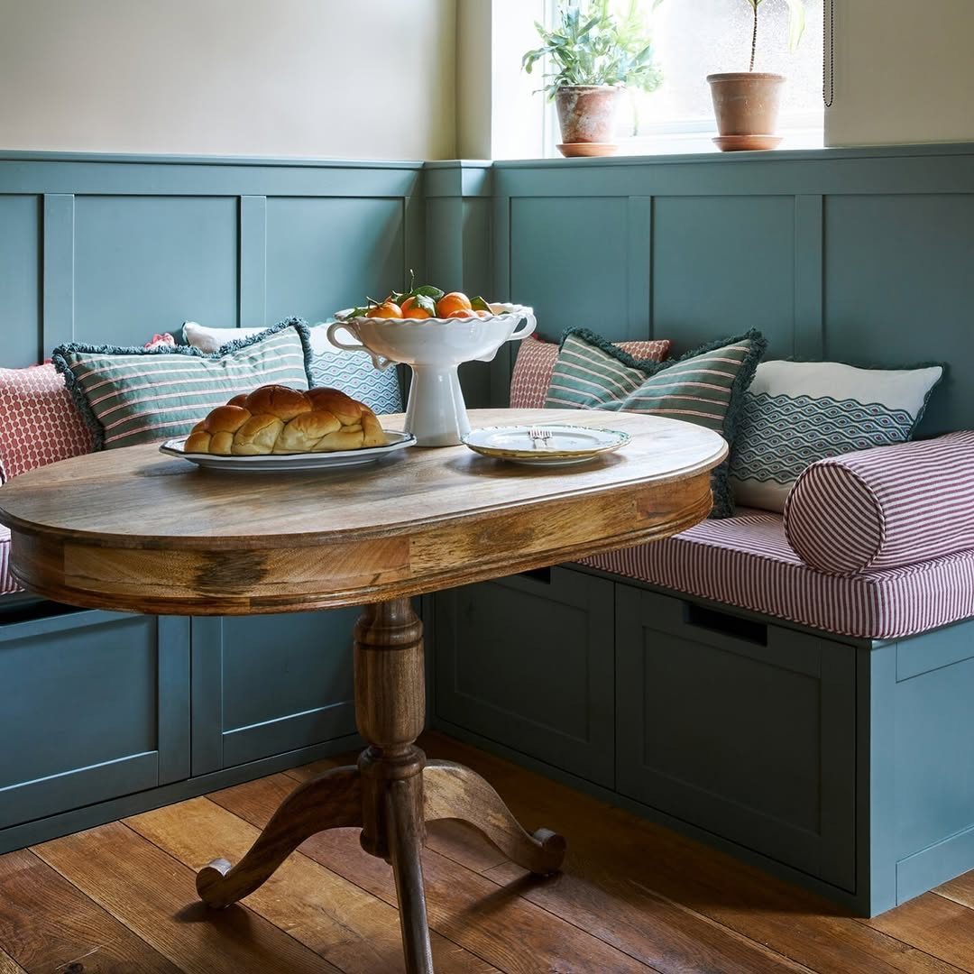 Round wooden pedestal table in a dining nook with teal blue built-in bench seating.