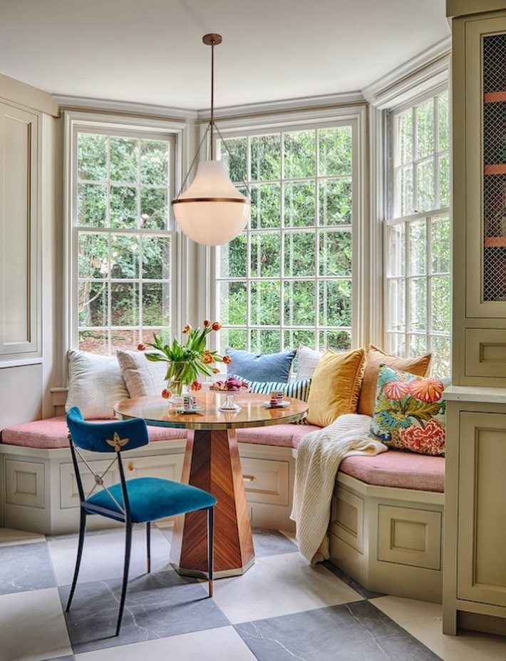 Round wooden dining table with a built-in banquette seating area in a bay window.