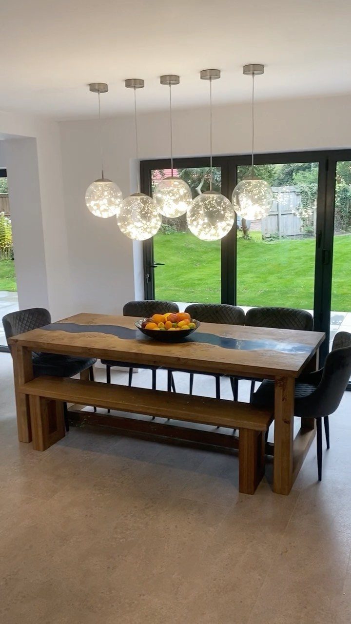 Wooden dining table with dark resin inlay, matching bench, and spherical pendant lights.