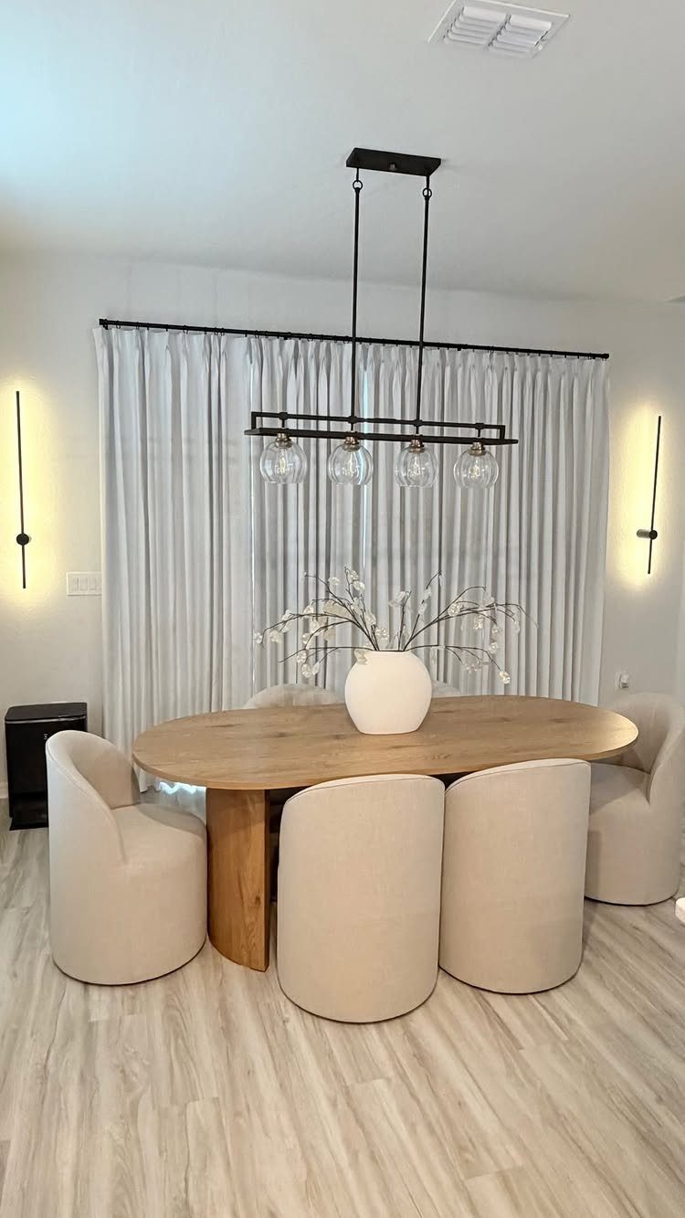 Oval wooden dining table with cream upholstered chairs and a modern linear chandelier.