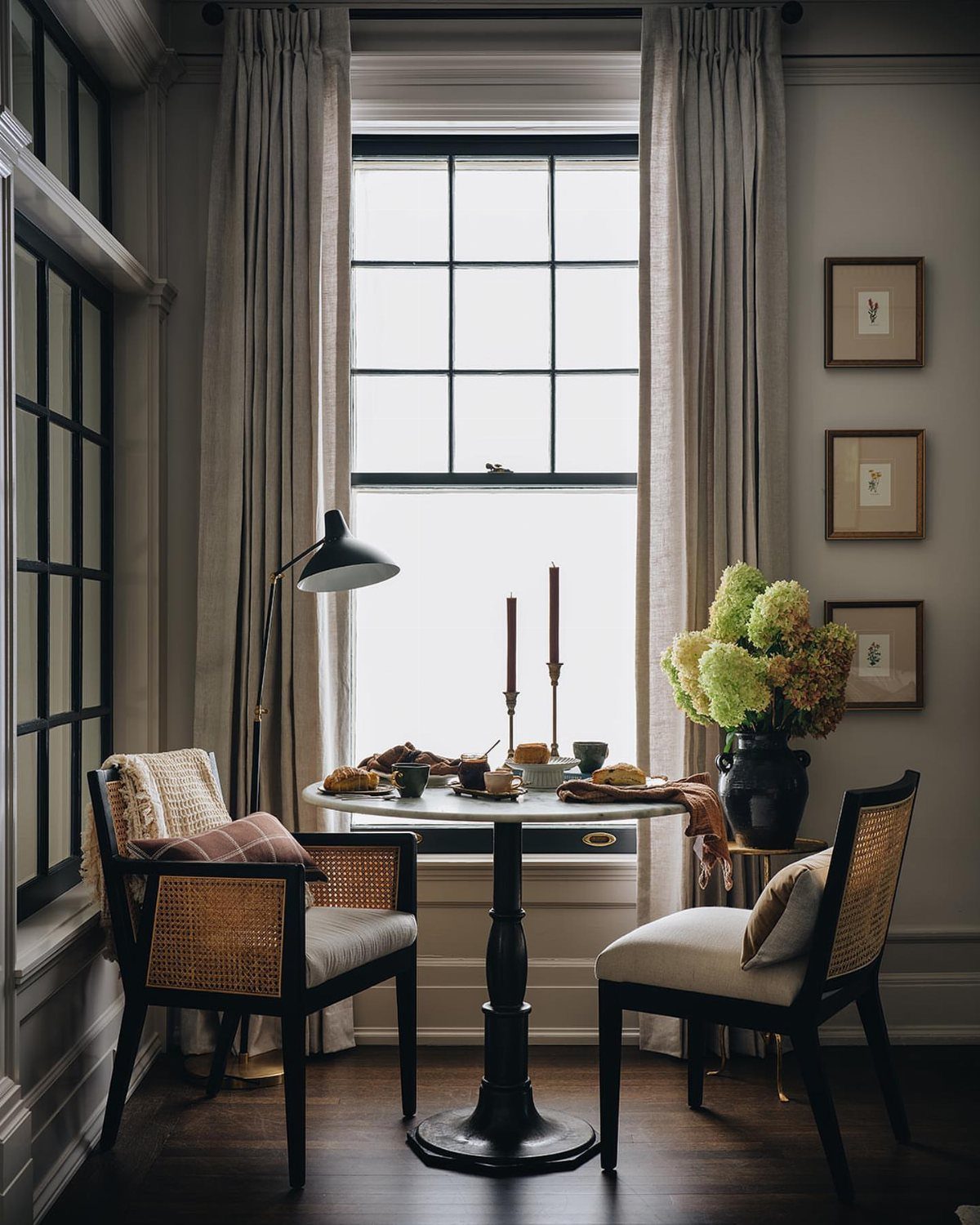 Small round bistro table with two cane chairs by a bright window.
