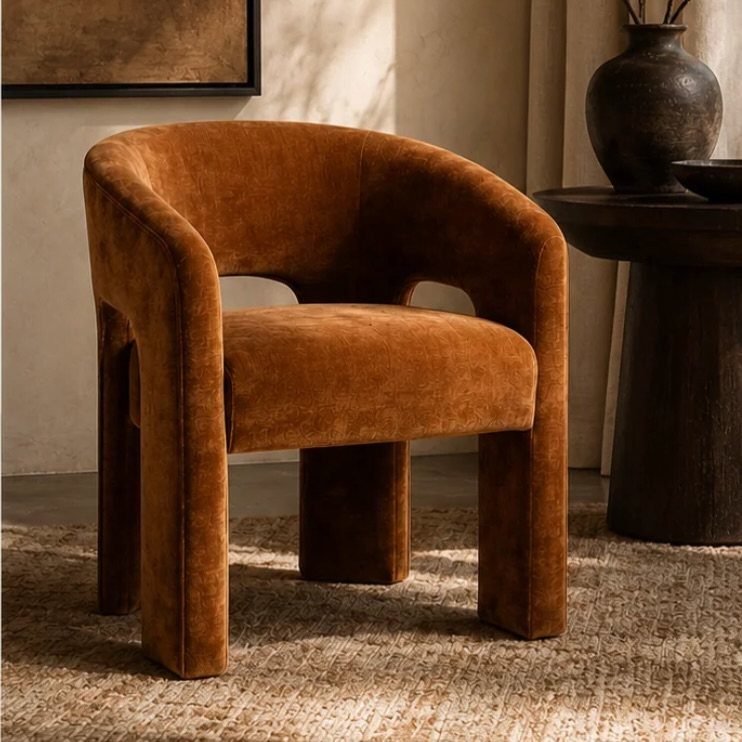 Tan velvet barrel-back chair with thick upholstered legs on a textured beige rug.