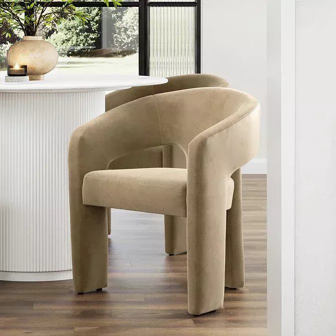 Tan velvet barrel-back chairs with sculptural curved frames next to a white fluted table.