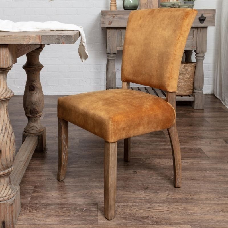 Tan velvet dining chair with a wooden frame next to a rustic table.