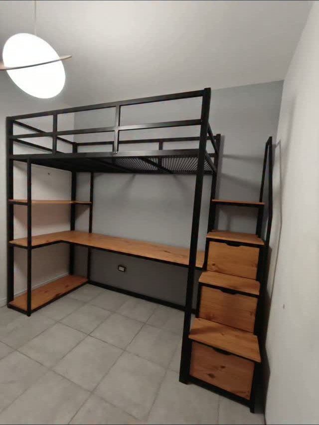 Black metal loft bed with integrated wooden desk and storage stairs in a room.