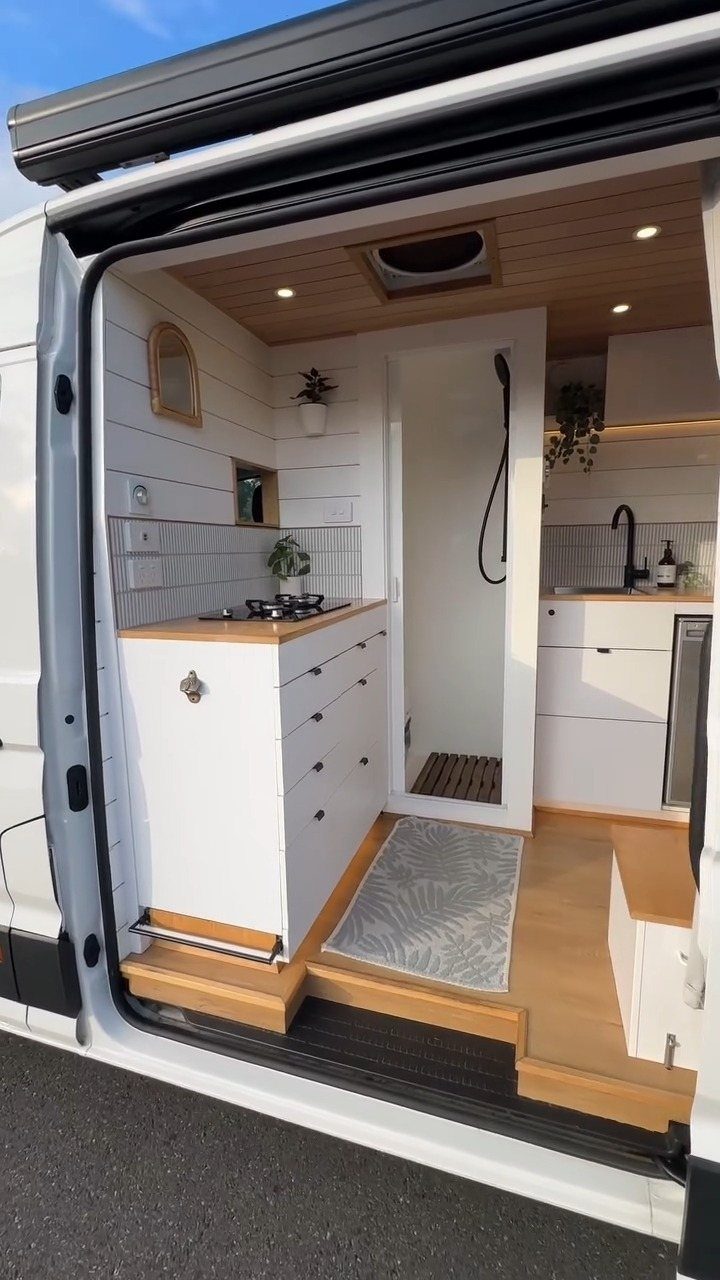 Camper van interior with white built-in kitchen cabinets and light wood finishes.