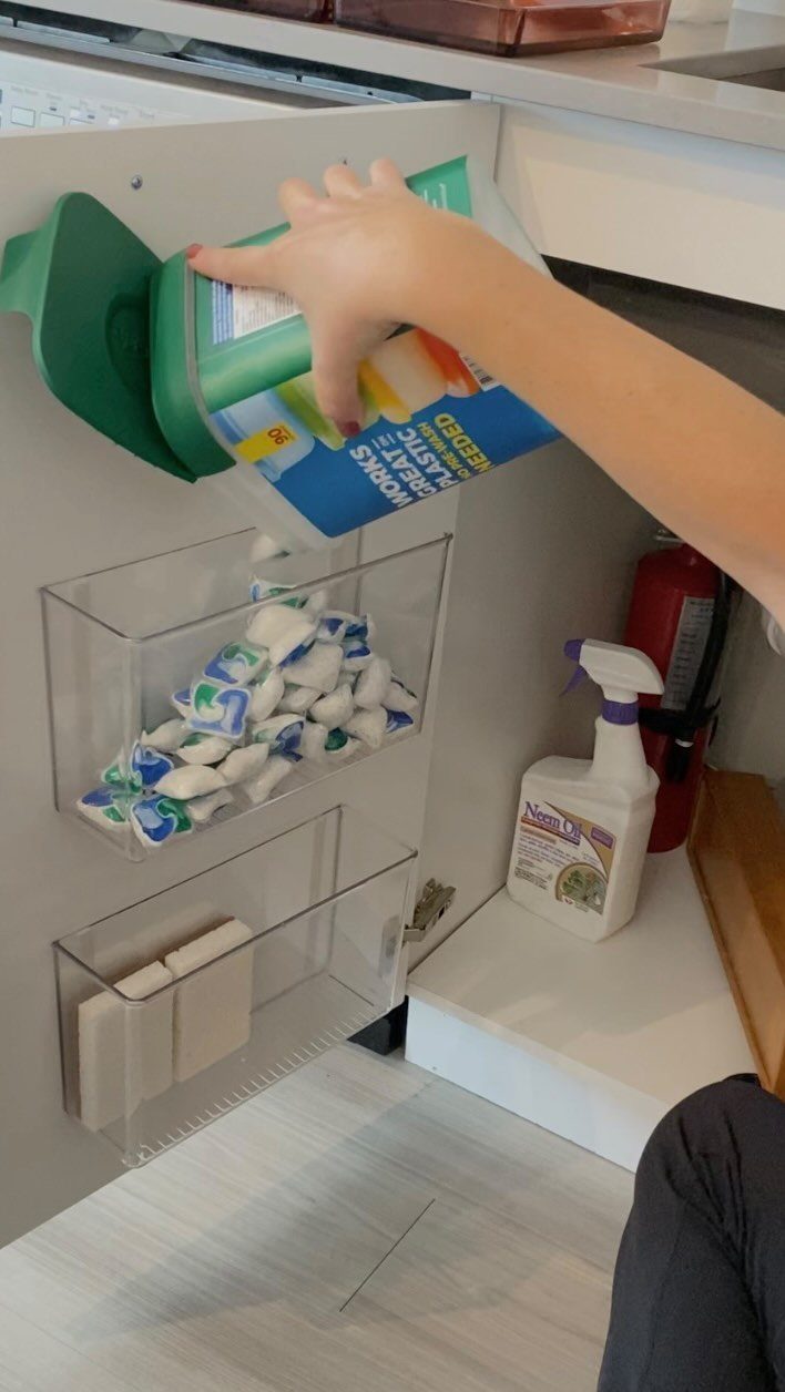 Clear plastic organizers mounted on a cabinet door holding cleaning supplies and wipes.