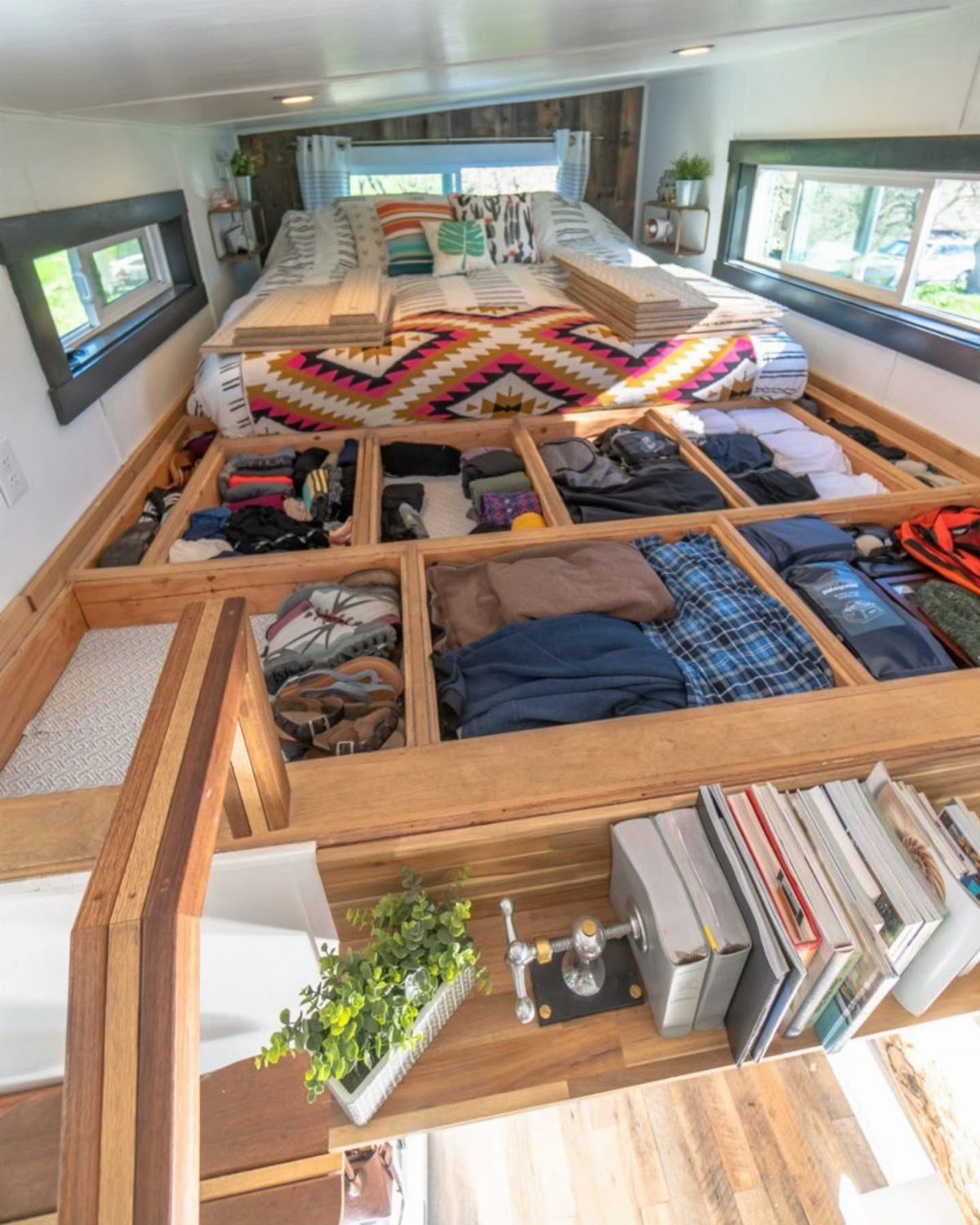 Underfloor storage compartments filled with clothes beneath a bed in a tiny home.