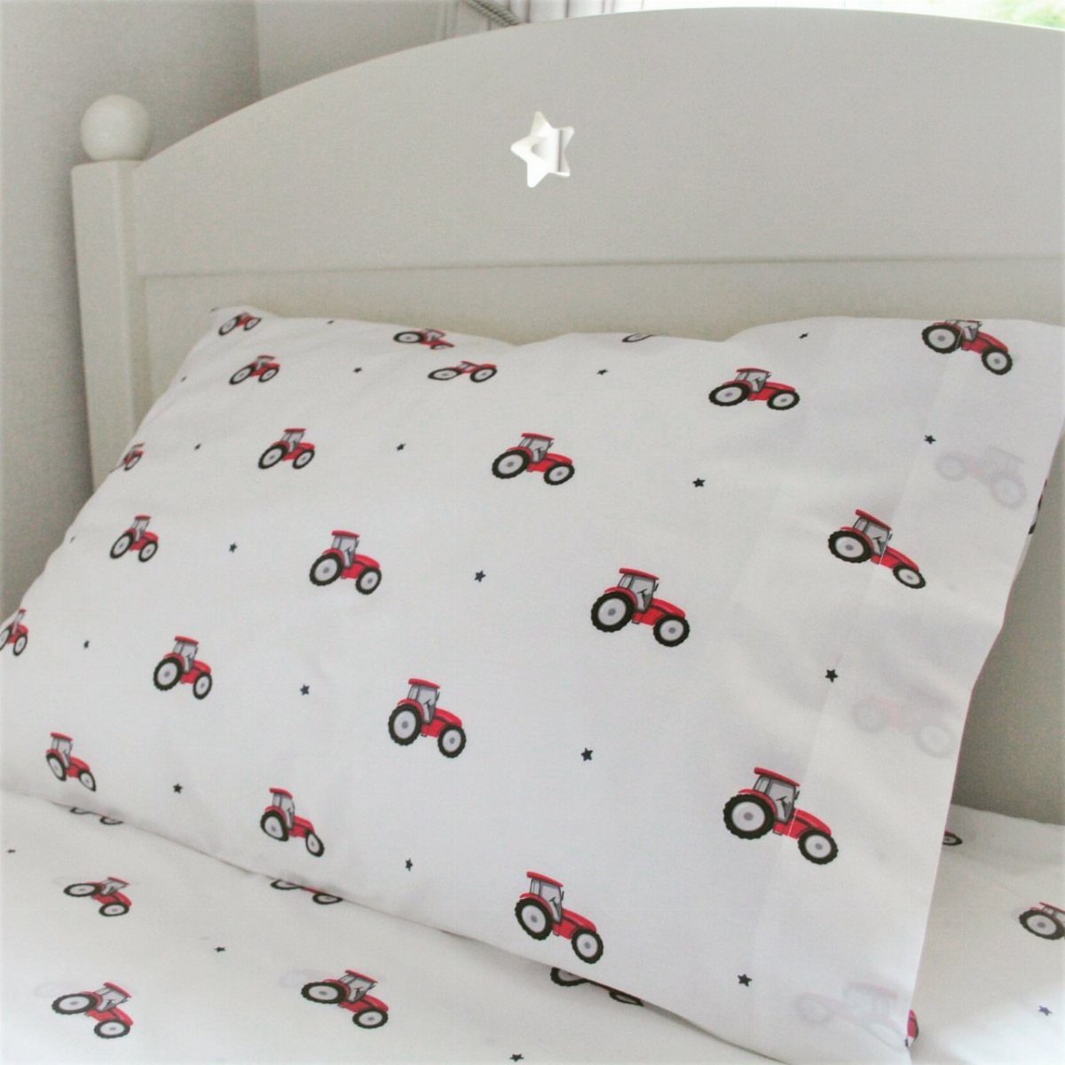 White bedding with a repeating pattern of small red tractors and black stars.