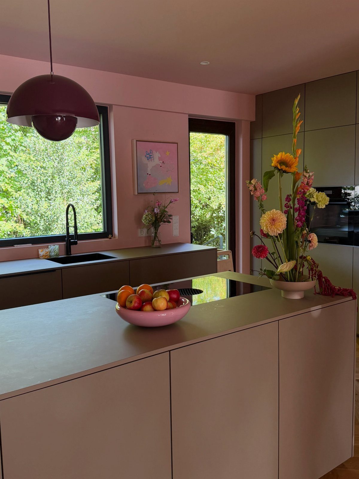 Two tone kitchen with pink island and mauve cabinets and floral arrangement.