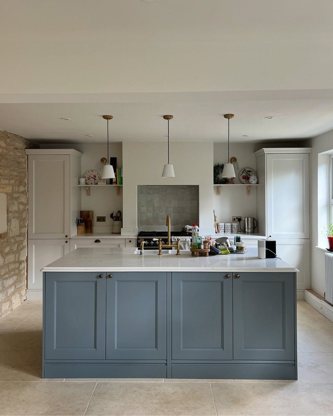 Blue kitchen island with white countertops and white perimeter cabinets in a bright room.
