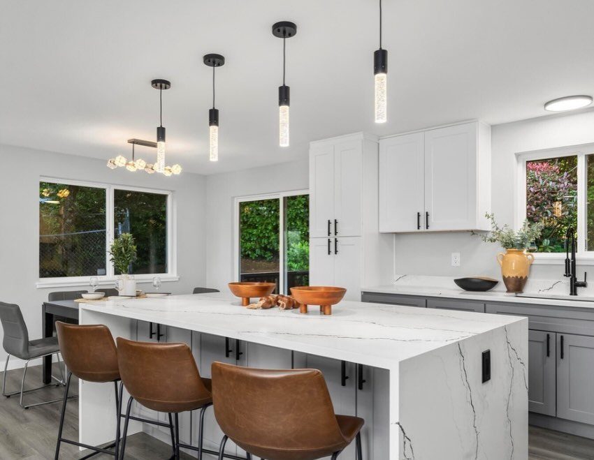 White upper cabinets and gray lower cabinets in a modern kitchen with marble countertops.