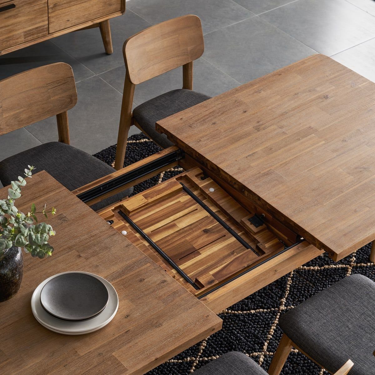 Extendable walnut dining table showing the internal sliding leaf and grey upholstered chairs.