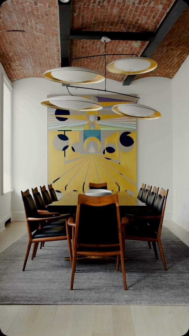 Walnut dining table with black leather chairs in a modern room with abstract art.