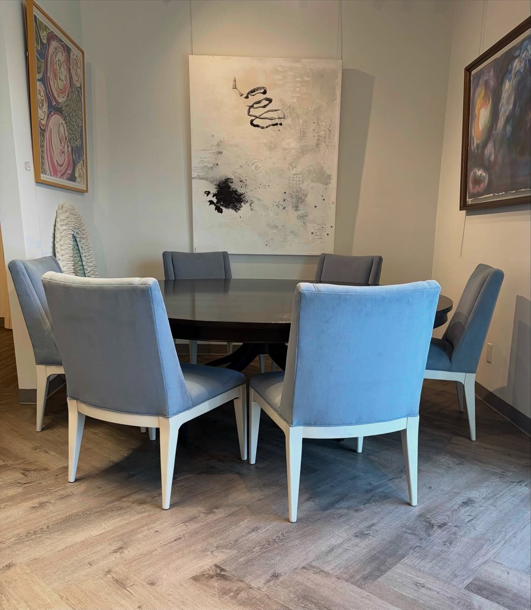 Dark walnut dining table with six light-blue upholstered chairs on herringbone wood floors.