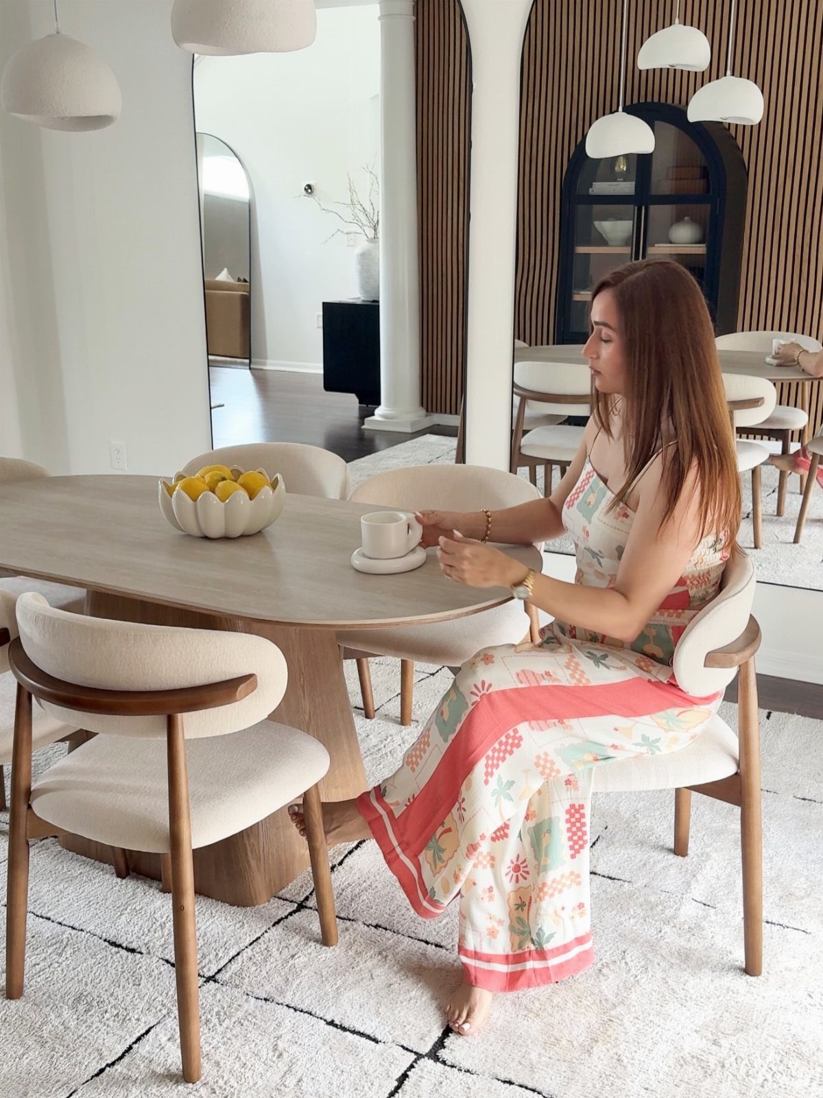 Oval walnut dining table with cream upholstered chairs and a woman sitting.