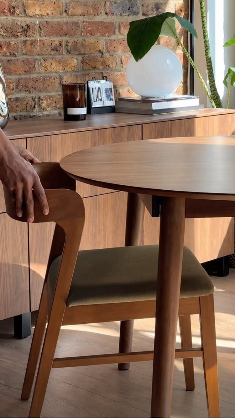 Round walnut dining table with a matching curved-back chair and green seat.