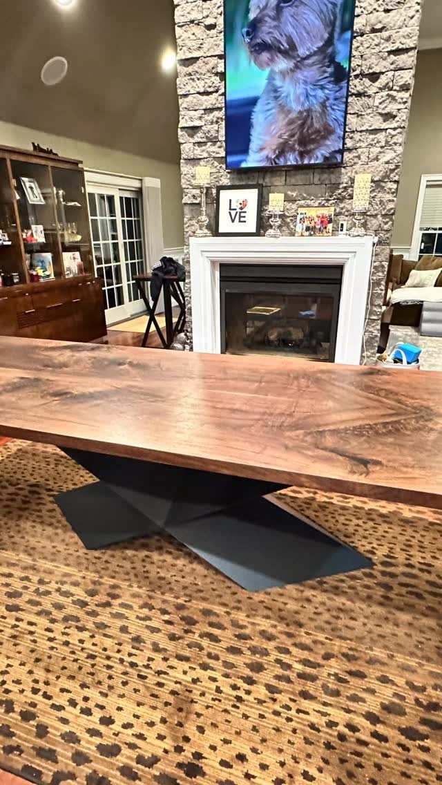 Walnut dining table with a black geometric base on a leopard print rug.