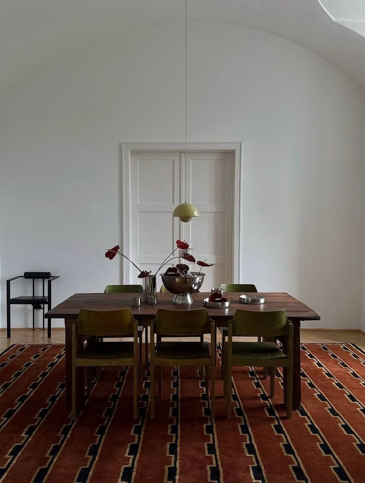 Walnut dining table with green chairs on a red and black patterned rug.