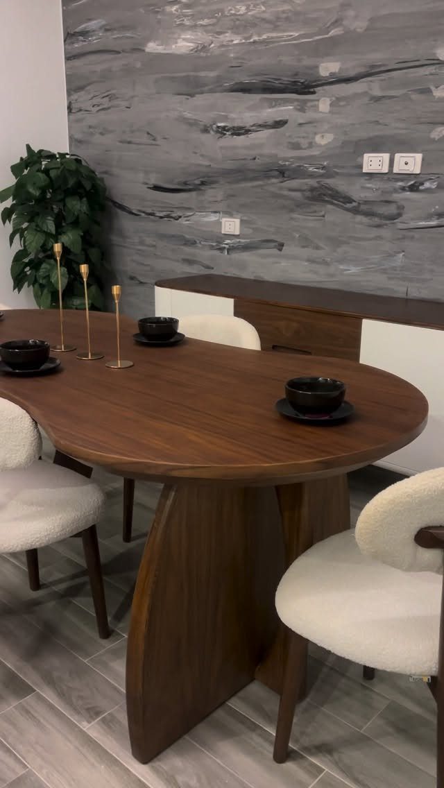 Oval walnut dining table with white chairs and a matching sideboard against marbled wall